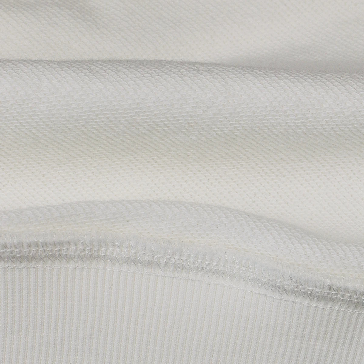 The close-up image presents the textured fabric of a white Retro Unisex Heavyweight Oversized sweatshirt by PODpartner, featuring Asia Spirit Japan Design. It showcases two distinct knitting patterns: a fine, smooth texture on the upper section and a ribbed knit on the lower, emphasizing the contrasting textures.